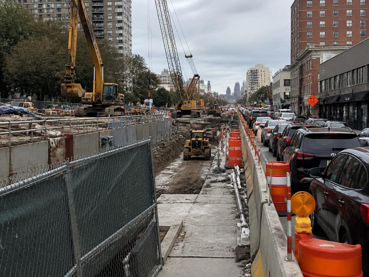A subway construction site with excavators, fenced hoarding and traffic detoured around the street