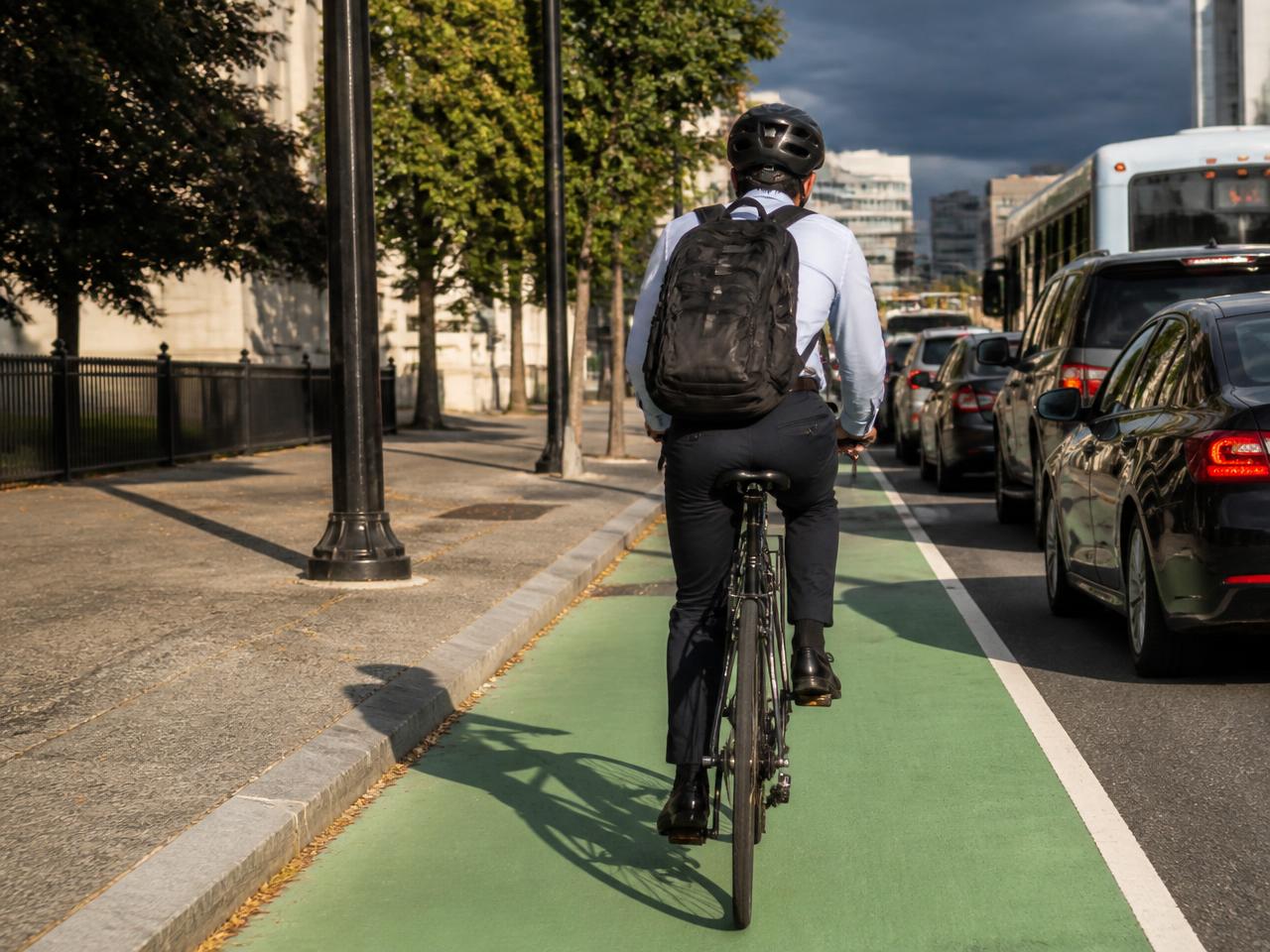 A commuter in office clothes cycling in a painted bike lane past stopped traffic with rain clouds ahead