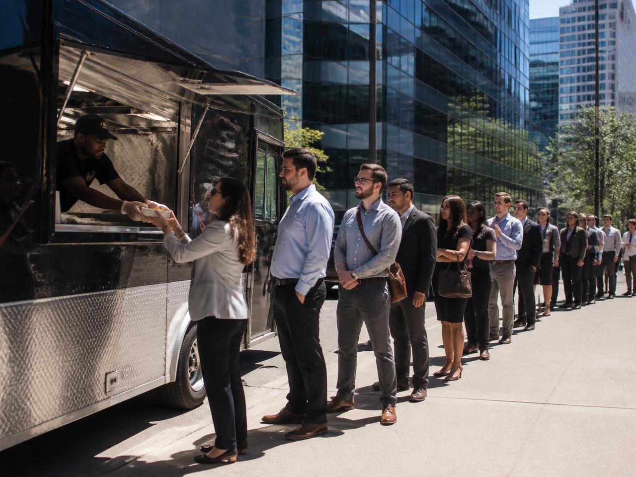 A food truck outside office towers at lunchtime with a long line of office workers waiting to be served